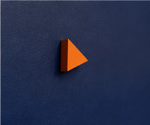 Macro view of a single orange triangle standing out from the blue surface, the only warm colour on the panel